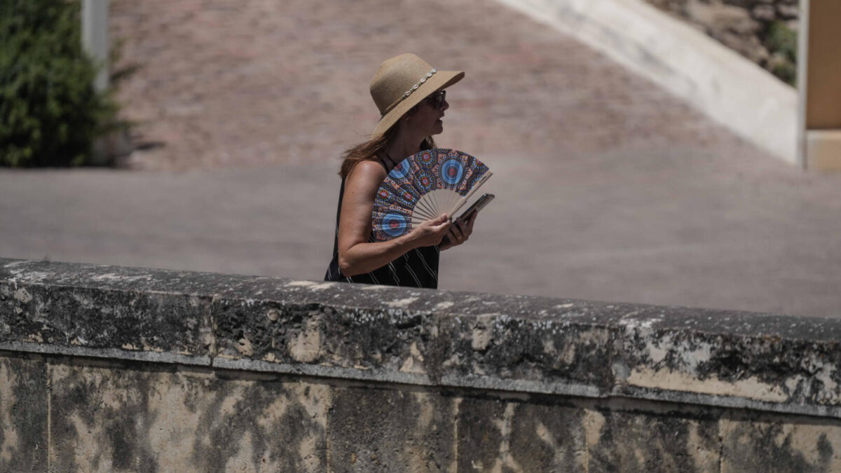 Una mujer hace frente a las altas temperaturas usando sombrero y abanico para refrescarse