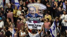 Un manifestante sostiene un cartel con una caricatura del Primer Ministro israelí, Benjamin Netanyahu, leyendo "El golpe de Michel Platini" mientras miles de manifestantes que apoyan a las familias de los rehenes israelíes retenidos por Hamas en Gaza participan en una manifestación de protesta frente al cuartel general militar de Kyria en Tel Aviv, Israel, 01 de septiembre de 2024.