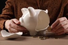 Una mujer sostiene una moneda de dos euros cerca de una hucha rota