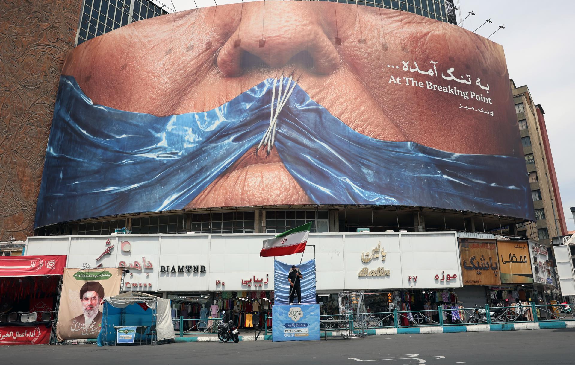 TEHRAN (IRAN(Islamic Republic Of)), 28/05/2026.- A man holds Irans national flag in front of a large anti-US billboard featuring US President Donald Trump and the Strait of Hormuz at Valiasr Square in Tehran, Iran, 28 May 2026. US President Donald Trump recently announced that a potential peace agreement to end the conflict and reopen the Strait of Hormuz has been largely negotiated through Pakistani mediators. However, the US has since launched new strikes in southern Iran. (Teherán) EFE/EPA/ABEDIN TAHERKENAREH RESTRICTIONS: NO Access Israel Media/Persian Language TV Stations Outside Iran/Strictly No Access BBC Persian/VOA Persian/Manoto TV/Iran International TV. (As mandated by Iran's Directorate General for Foreign Media) --