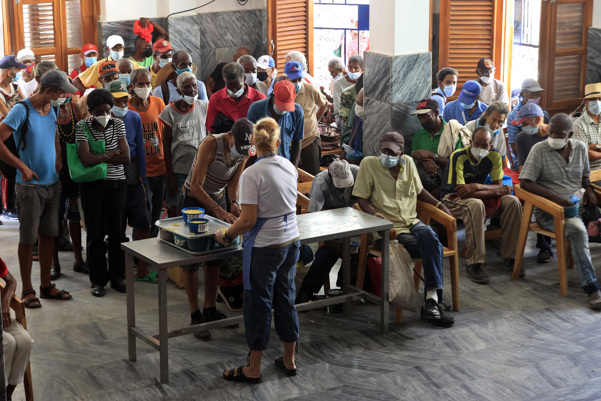 AME5740. LA HABANA (CUBA), 28/05/2026.- Personas reciben alimentos por personal de la ONG Quisicuaba este lunes, en La Habana (Cuba). Delgadísimos y agotados, los ancianos esperan pacientemente a escuchar su número para recoger un pozuelo de comida caliente de la cocina social de la mayor ONG de Cuba. Son más de un centenar y no paran de llegar más. EFE/ Ernesto Mastrascusa