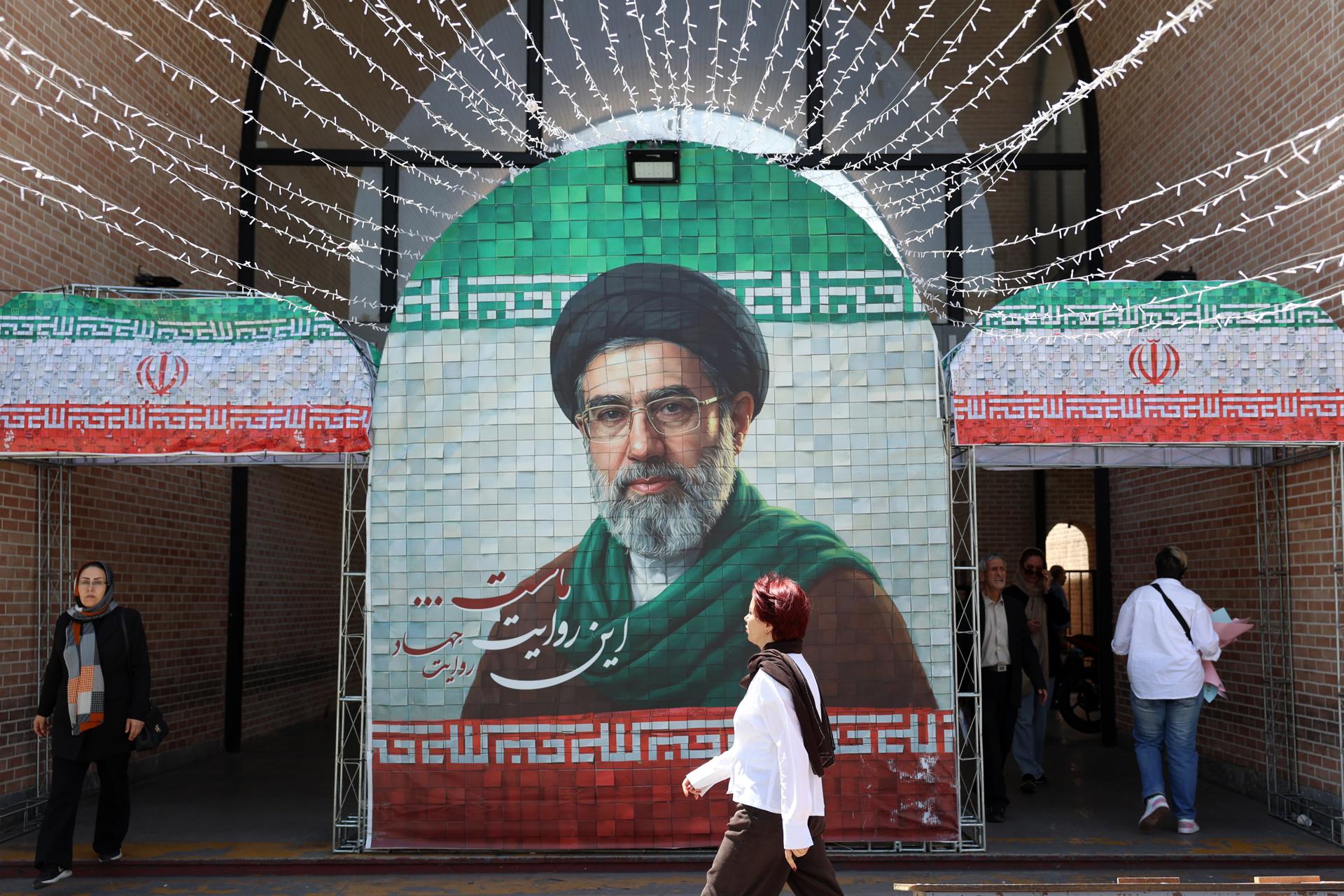 TEHRAN (Iran (Islamic Republic Of)), 06/05/2026.- Iranians walk next to a picture of Iran supreme leader Ayatollah Mojtaba Khamenei in a street in Tehran, Iran, 06 May 2026. US President Donald Trump announced pausing the operation of escorting ships through the Strait of Hormuz, hinting at progress in peace talks with Tehran. (Teherán) EFE/EPA/ABEDIN TAHERKENAREH