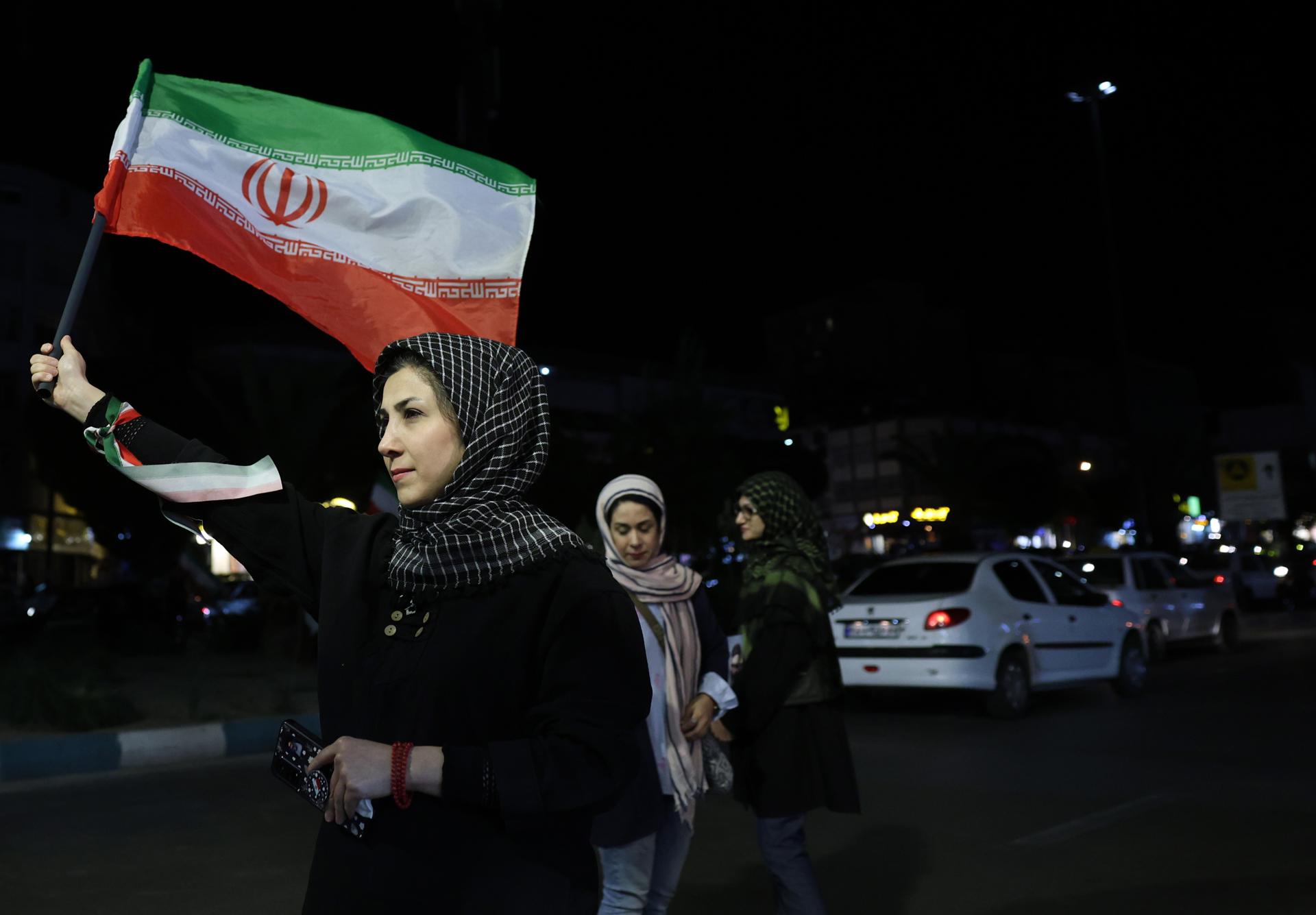 TEHRAN (IRAN(Islamic Republic Of)), 20/05/2026.- A woman holds Irans national flag during a gathering in support of the Iranian government against the US and Israel, in a street in Tehran, Iran, 20 May 2026. Tensions between the US and Iran continue as a deal has not been reached and ships continue to be unable to pass the Strait of Hormuz. (Teherán) EFE/EPA/ABEDIN TAHERKENAREH