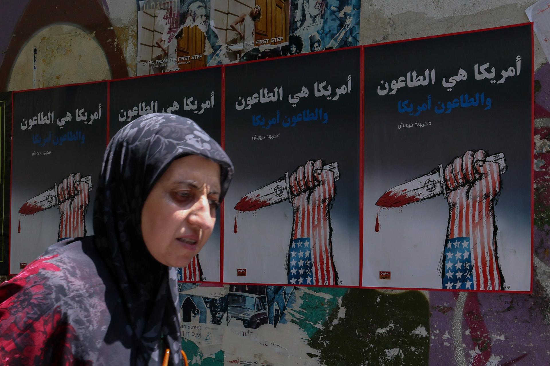 FOTODELDÍA BEIRUT (Líbano), 09/06/2026.- Una mujer pasa junto a carteles políticos colgados en la pared de una calle de Beirut, Líbano, este martes. Los carteles muestran una mano decorada con los colores de la bandera estadounidense sosteniendo una daga que simboliza a Israel y con el lema «Estados Unidos es una plaga, y la plaga es Estados Unidos». El Ministerio de Salud libanés informó que, hasta el 8 de junio, los ataques israelíes en todo el Líbano habían causado la muerte de más de 3.637 personas y dejado más de 11.188 heridos desde que se reanudaron las hostilidades entre Israel y Hezbolá. EFE/ Wael Hamzeh