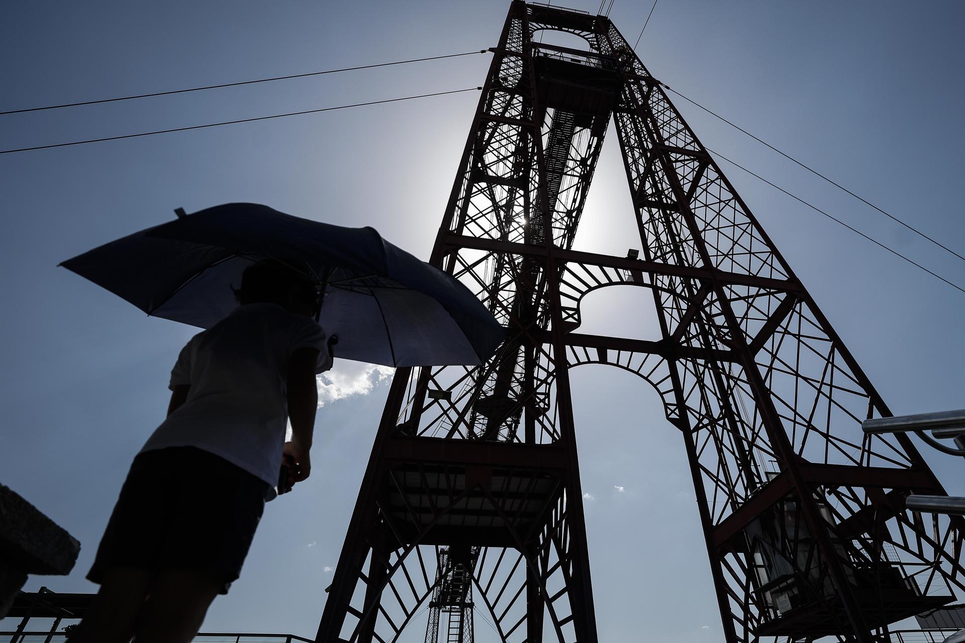 FOTODELDÍA - GETXO (BIZKAIA), 24/06/2026.- Un joven se protege del sol con un paragüas frente al Puente de Bizkaia en Getxo (Bizkaia) este miércoles, jornada en que la ola de calor que azota Euskadi ha vuelto a situar las temperaturas por encima de los 40 ºC en numerosos puntos del territorio. A las 16:00 horas la temperatura máxima se ha registrado en Zizurkil (Gipuzkoa) y Sodupe (Bizkaia) con 44 ºC, según los datos de la Agencia Vasca de Meteorología, Euskalmet. EFE/Miguel Toña
