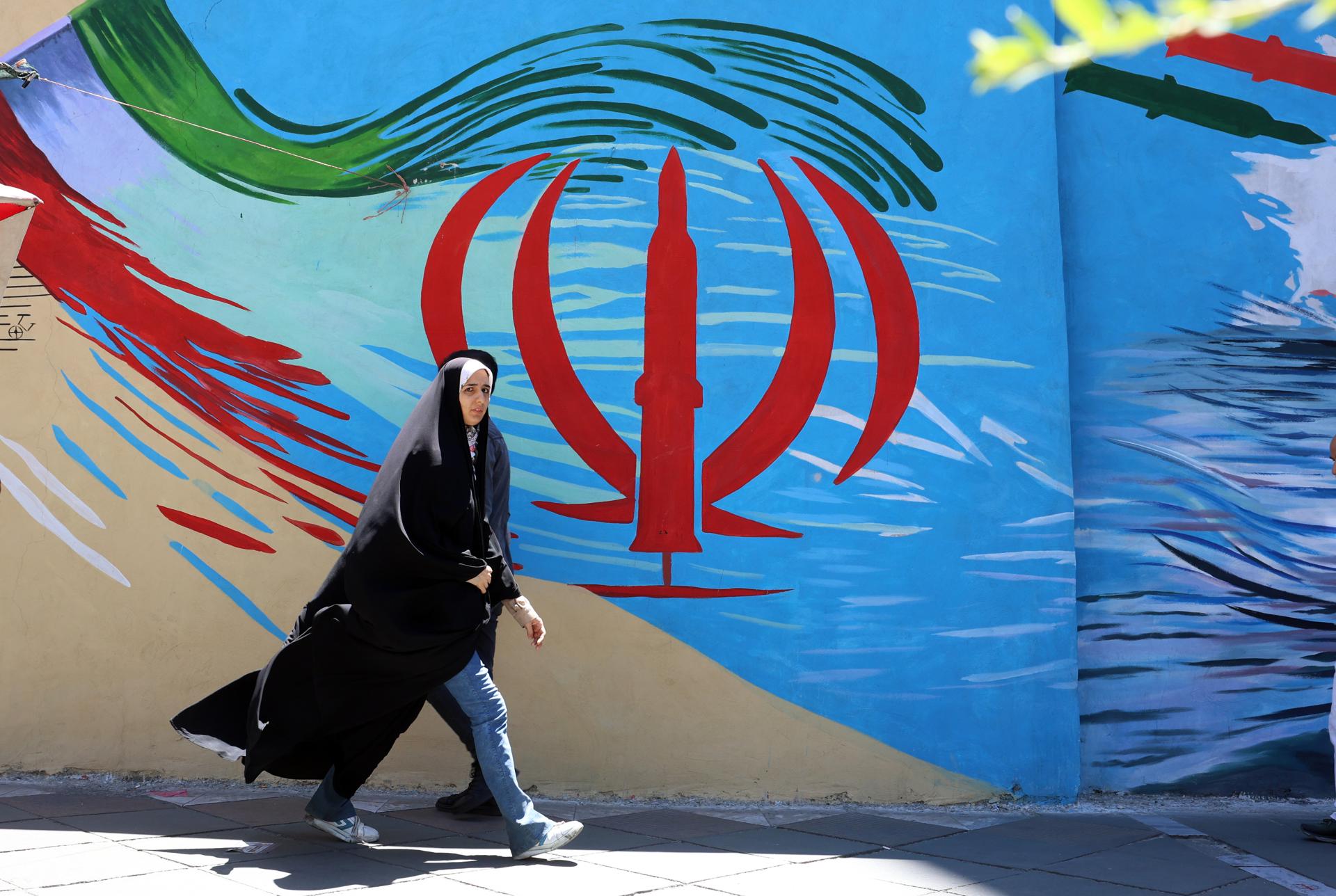 TEHRAN (Iran (Islamic Republic Of)), 15/06/2026.- A veiled Iranian woman walks past a wall painting of Iran's national flag on a street in Tehran, Iran, 15 June 2026. US President Donald Trump announced on his social media platform that a deal with Iran has been reached and is set to be signed on 19 June in Switzerland. (Suiza, Teherán) EFE/EPA/ABEDIN TAHERKENAREH RESTRICTIONS: NO Access Israel Media/Persian Language TV Stations Outside Iran/Strictly No Access BBC Persian/VOA Persian/Manoto TV/Iran International TV. (As mandated by Iran's Directorate General for Foreign Media) --