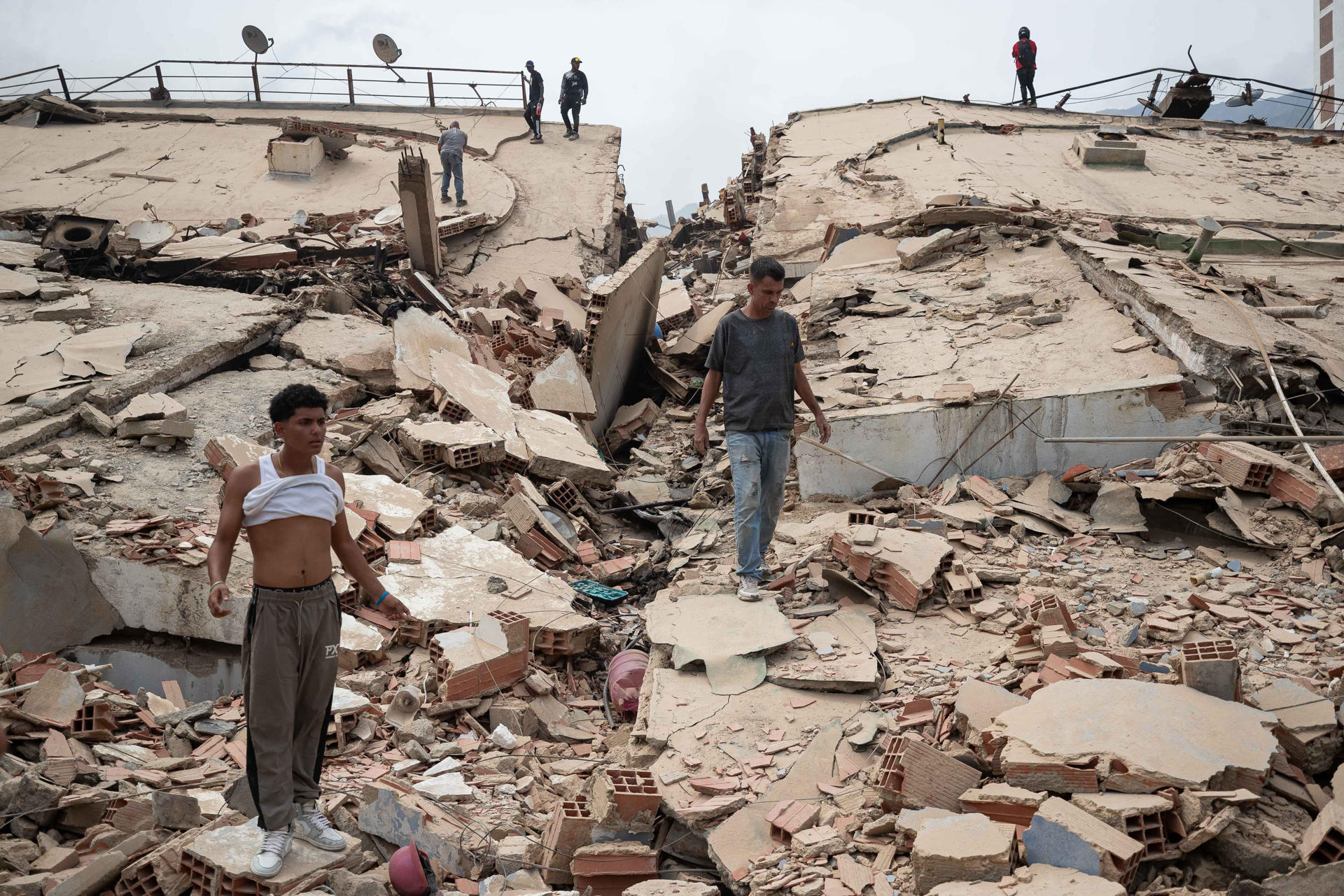 AME4353. LA GUAIRA (VENEZUELA), 25/06/2026.- Personas caminan por escombros de edificios afectados por terremotos este jueves, en La Guaira (Venezuela). El número de fallecidos en Venezuela a causa de los dos terremotos del miércoles se elevó a 188 y el de heridos a 1.520, mientras que al menos 346 construcciones, entre edificios, hospitales y centros comerciales, resultaron afectadas, informó el presidente de la Asamblea Nacional (AN, Parlamento), el chavista Jorge Rodríguez. EFE/ Ronald Peña R.