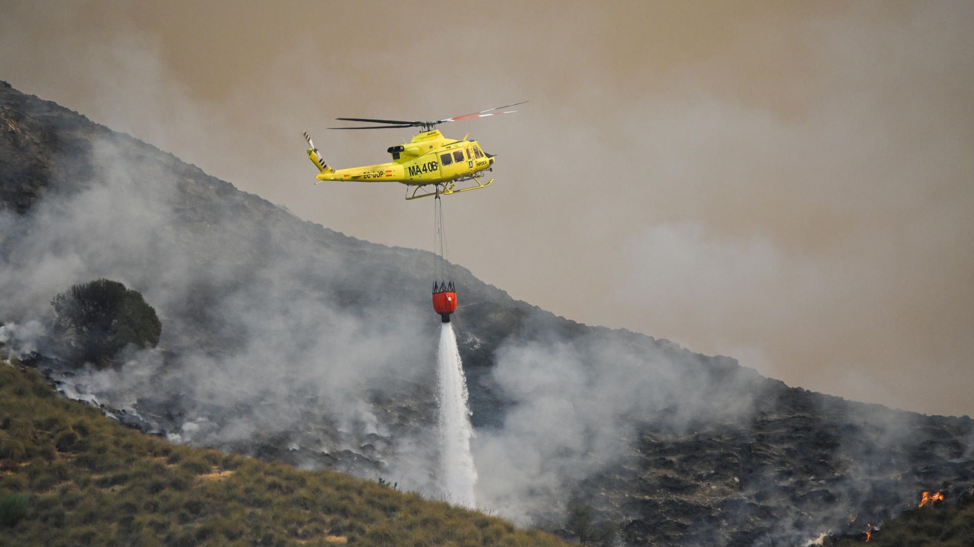 Un helicóptero del servicio de extinción de incendios arroja este viernes agua sobre uno de los focos del incendio forestal declarado en Los Gallardos.