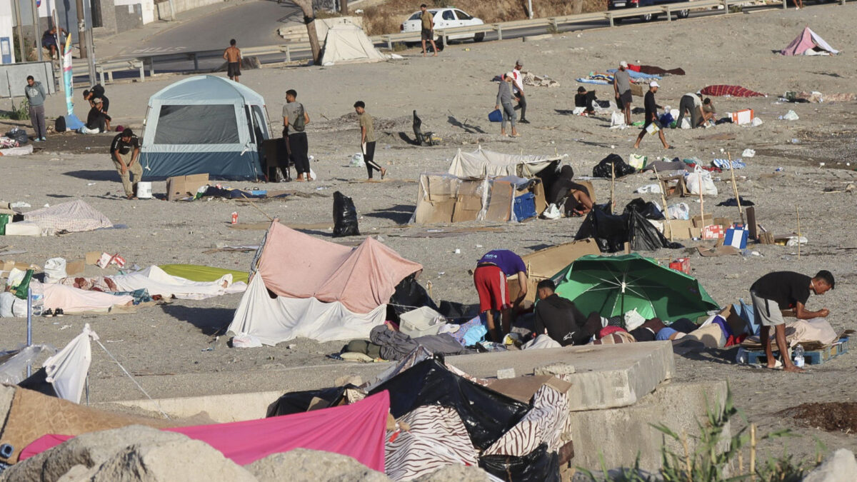 CEUTA, 24/08/2026.- Varios migrantes permanecen este lunes acampados en la playa de El Trampolín de Ceuta. La situación en Ceuta tras la entrada masiva de migrantes del 30 de julio sigue acaparando el foco en una jornada en la que el Ministerio de Sanidad reúne a las comunidades autónomas para activar el mecanismo de solidaridad que facilitará la donación de vacunas, mientras el secretario de Estado de Sanidad viaja a la ciudad autónoma para analizar la situación sanitaria. EFE/ Reduan