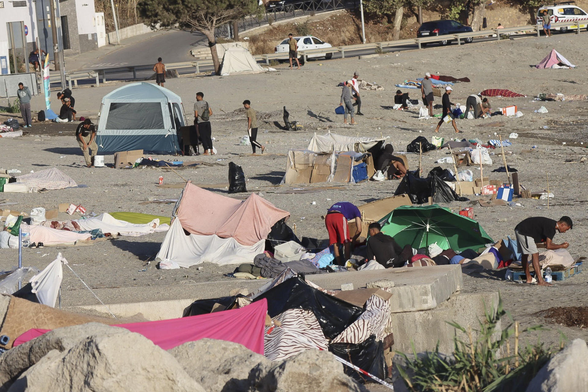 CEUTA, 24/08/2026.- Varios migrantes permanecen este lunes acampados en la playa de El Trampolín de Ceuta. La situación en Ceuta tras la entrada masiva de migrantes del 30 de julio sigue acaparando el foco en una jornada en la que el Ministerio de Sanidad reúne a las comunidades autónomas para activar el mecanismo de solidaridad que facilitará la donación de vacunas, mientras el secretario de Estado de Sanidad viaja a la ciudad autónoma para analizar la situación sanitaria. EFE/ Reduan