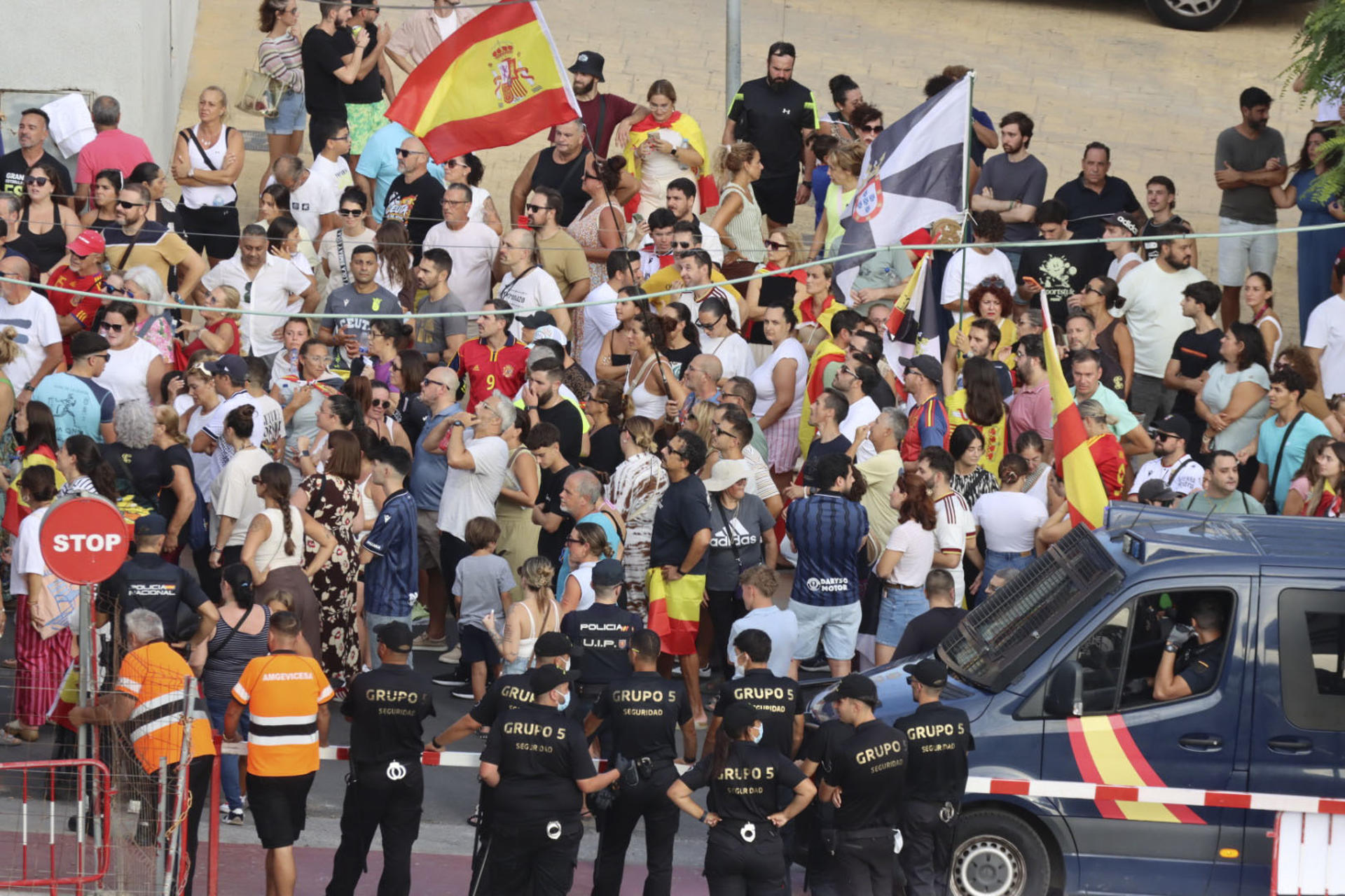 CEUTA, 27/08/2026.- Los migrantes recogen comida suministrada por voluntarios de Cruz Roja en la playa del Trampolín de Ceuta mientras la Policía Nacional impide que los manifestante lleguen al lugar donde se está llevando a cabo el reparto de las bolsas con alimentos EFE/Reduan