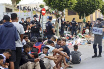 CEUTA, 31/08/2026.- Migrantes frente a la explanada de embotellamiento de Loma Colmenar donde hace casi dos semanas, se habilitó un campamento temporal para realojar a los migrantes pero de momento no es posible ya que no hay suficientes espacio para montar más carpas militares en la mencionada explanada. El Gobierno local de Ceuta y otros colectivos y organizaciones siguen reclamando la expulsión de los miles de migrantes que permanecen todavía en el territorio un mes después de la entrada de más de 70.000 personas a través de la frontera con Marruecos. EFE/Reduan