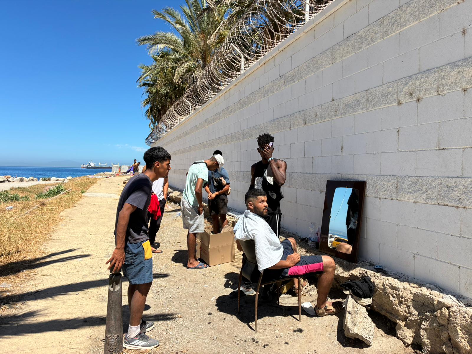 Jóvenes se cortan el pelo entre sí en una "barbería improvisada" en la playa del Trampolín, en Ceuta. María Serrano