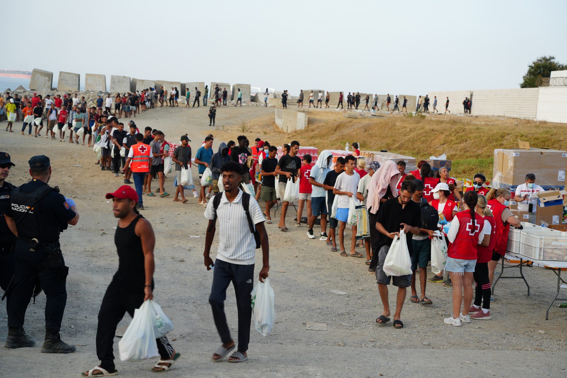 Colas de migrantes recogiendo comida en la playa de El Trampolín en Ceuta.