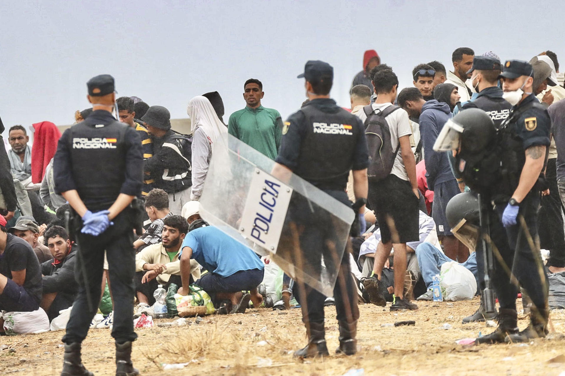 CEUTA, 21/08/2026.- La policía vigila a inmigrantes que continúan viviendo en las inmediaciones de la playa del Trampolín en Ceuta, este viernes. El secretario de Estado Juventud e Infancia, Rubén Pérez Correa, ha considerado "factible" llevar a cabo "en un plazo de pocas semanas" el traslado de 500 niñas migrantes no acompañadas desde Ceuta a la Península y, para ello, confía en la "voluntad" del Gobierno de la ciudad autónoma. EFE/Reduan