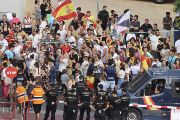 Los inmigrantes recogen comida suministrada por voluntarios de Cruz Roja en la playa del Trampolín de Ceuta mientras la Policía Nacional impide que los manifestantes lleguen al lugar donde se está llevando a cabo el reparto. EFE/Reduan