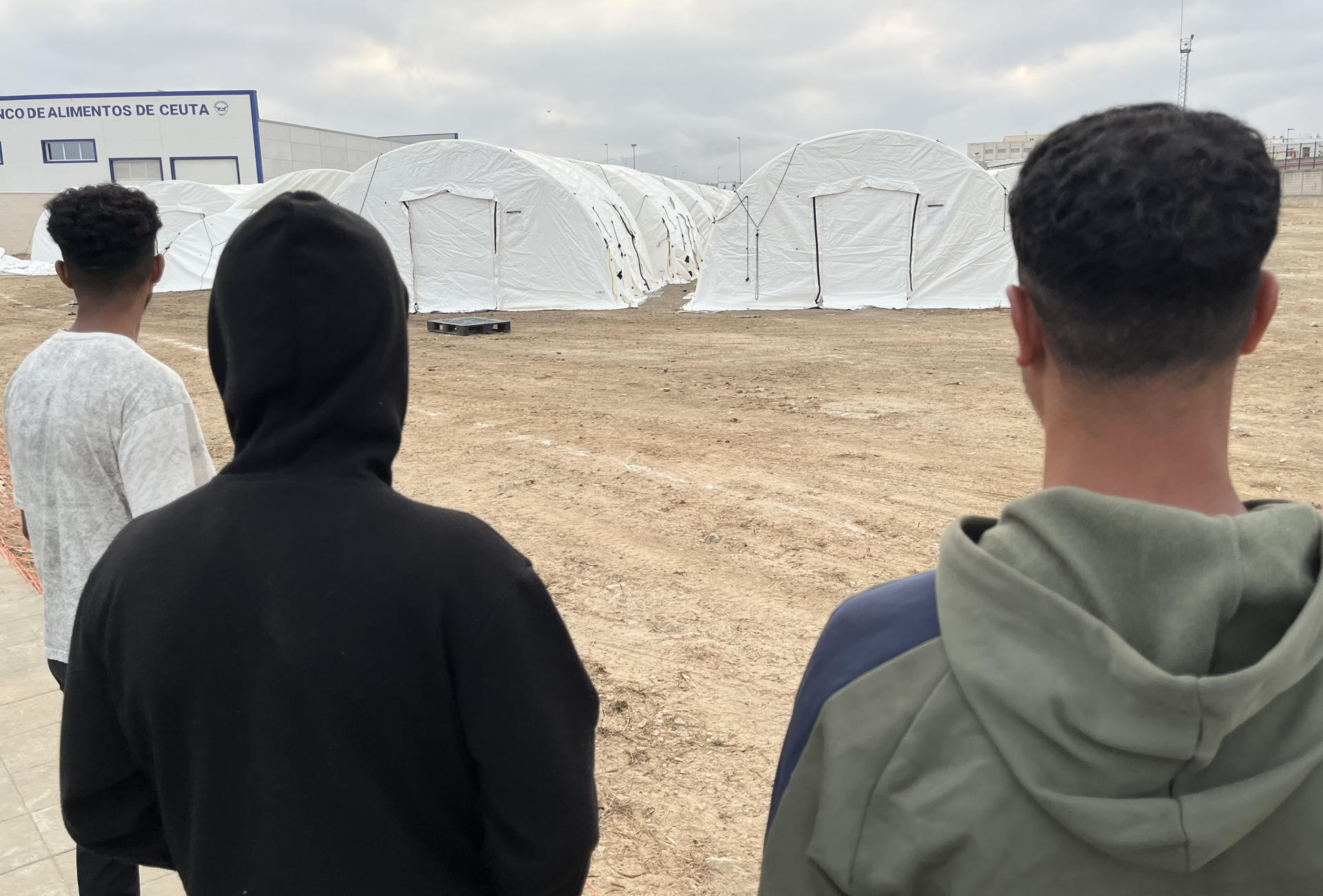 FOTODELDÍA CEUTA, 07/09/2026.- Tres jóvenes migrantes esperan en la mañana de este lunes para ser alojados en el nuevo campamento temporal que se está habilitando en el muelle de Poniente del puerto de Ceuta que previsiblemente entrará en funcionamiento mañana martes. EFE/Reduan