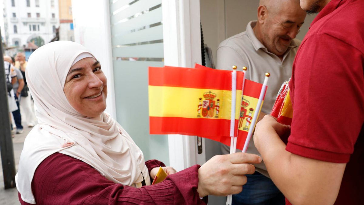 Una mujer reparte banderitas de España horas antes de la visita de los reyes.