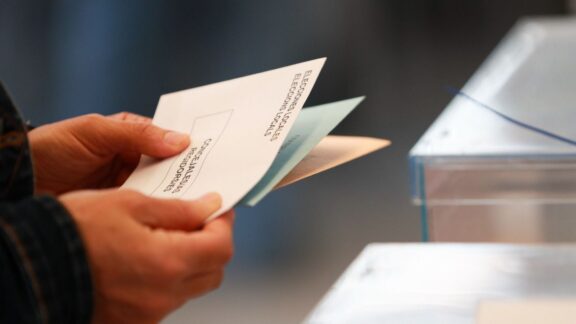 Una persona sostiene papeletas electorales frente a las urnas.