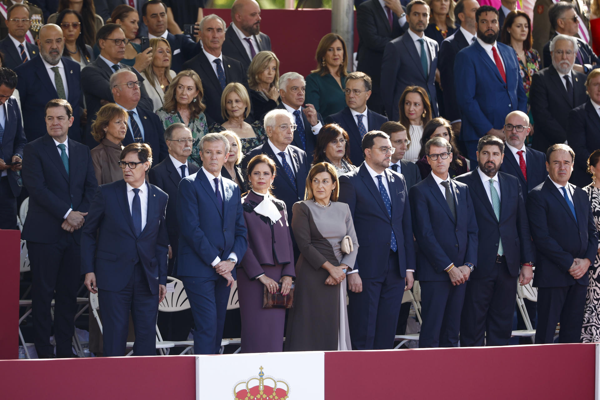 MADRID, 12/10/2026.- Los presidentes autonómicos de (de i a d) Cataluña, Salvador Illa; Galicia, Alfonso Rueda junto a su mujer, Marta Coloret; de Cantabria, María José Sáenz de Buruaga; de Asturias, Adrián Barbón; La Rioja, Gonzalo Capellán; Murcia, Fernando López Miras, y Valencia, Juan Francisco Pérez Llorca, durante el tradicional desfile militar por las calles del centro de Madrid en el que participan casi 4.400 militares, 144 vehículos, 39 motos, 50 aviones y 32 helicópteros, este lunes Día de la Fiesta Nacional.