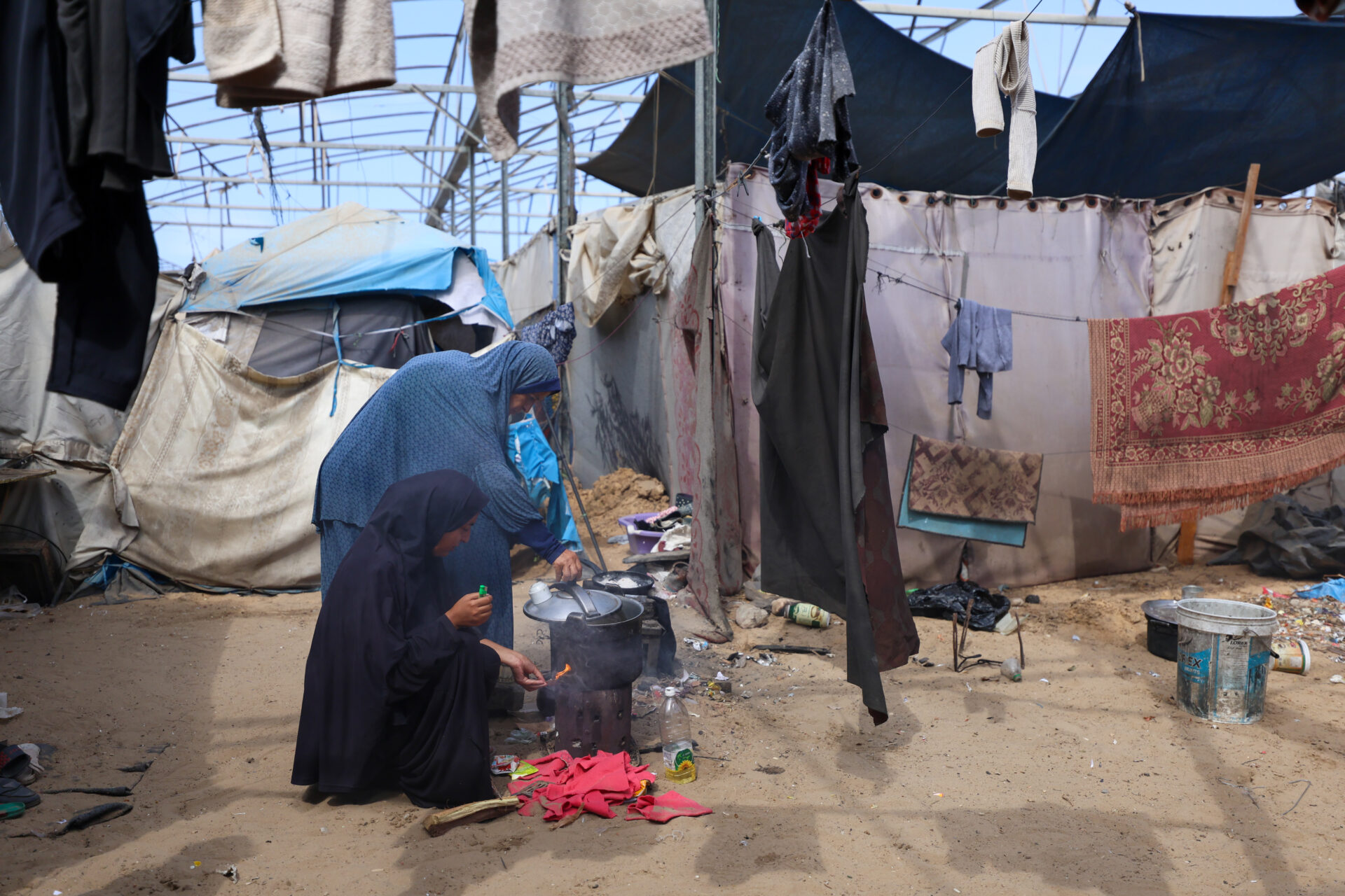 A displaced mother and her daughter prepare a meal over an open fire inside their tent in Mawasi, Khan Younis. With limited access to cooking gas or proper kitchen facilities, many families in the crowded coastal area are forced to rely on basic and hazardous methods to cook.