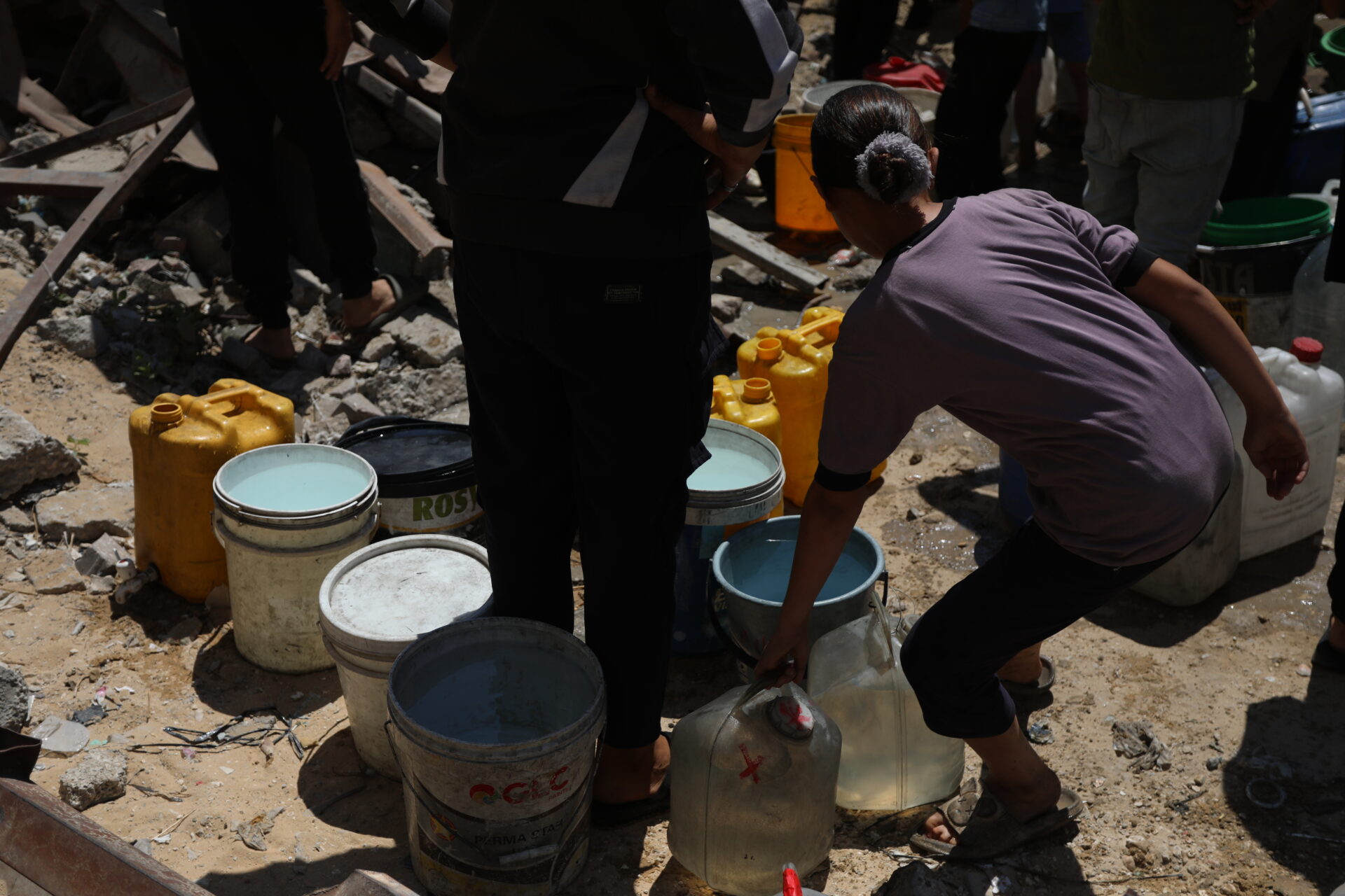 Palestinians wait with worn-out containers to fill them from a truck. The scarcity of water and the danger of collection create immense tension.