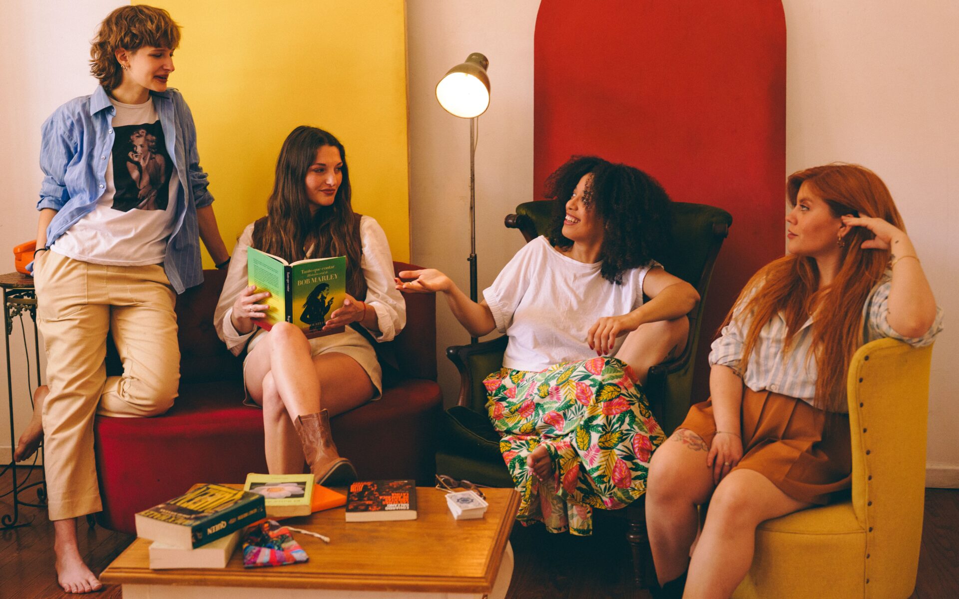 Cuatro amigas relajándose y divirtiéndose con libros y conversando en el interior.